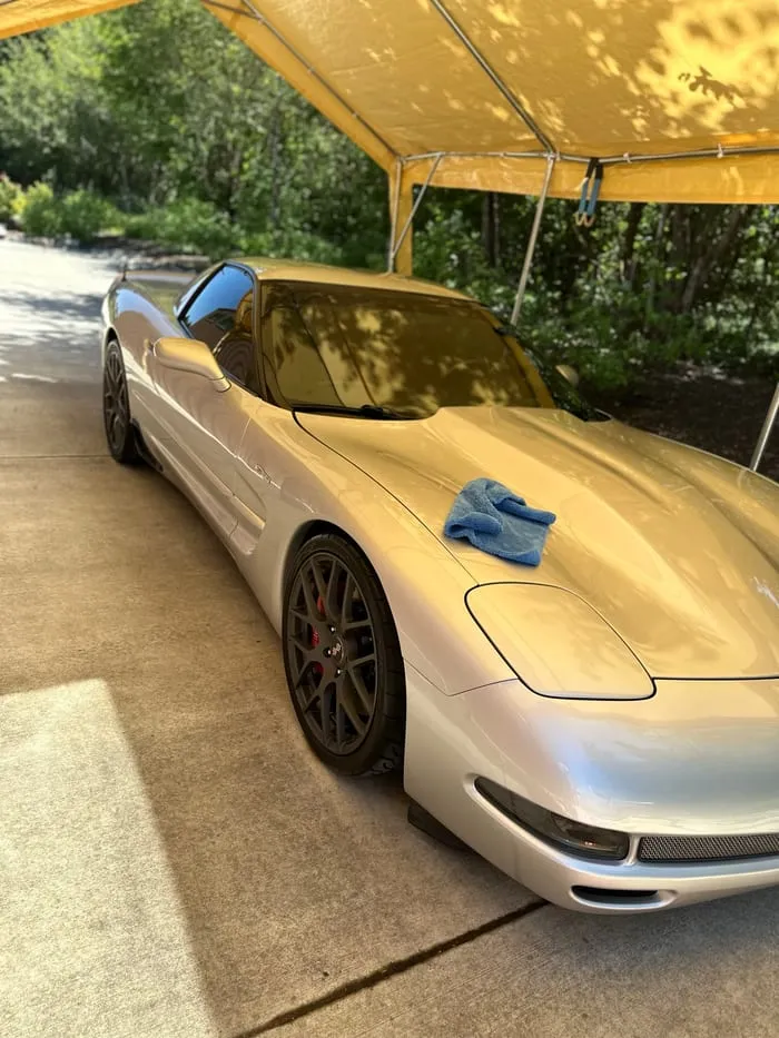 Gold C5 Corvette under a canopy with a microfibre towel resting on the hood mid-job