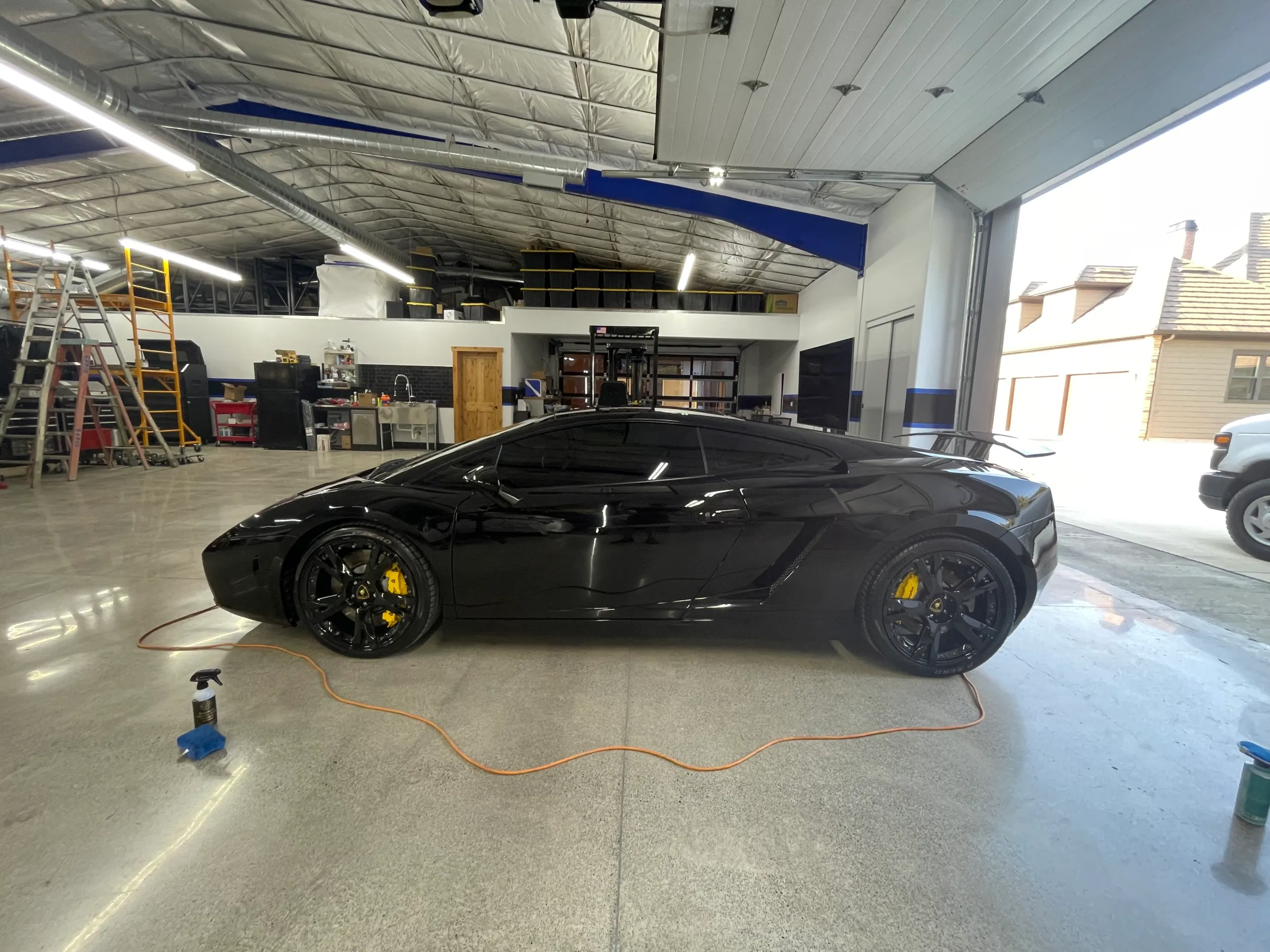 Black Lamborghini Gallardo side-on inside the detailing shop with the bay door open