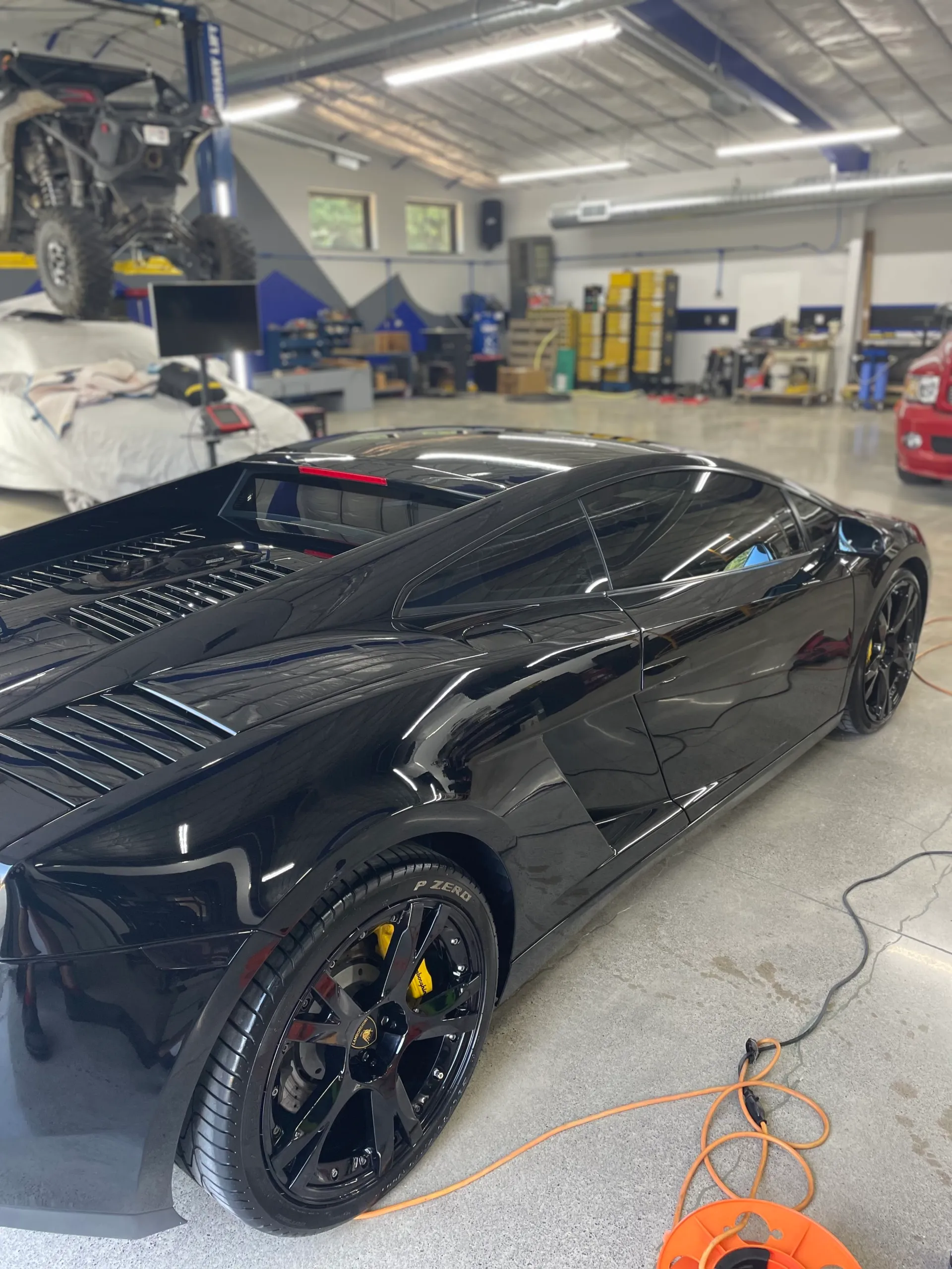 Polished black paint on a Lamborghini's rear quarter, shop lighting mirrored in the surface