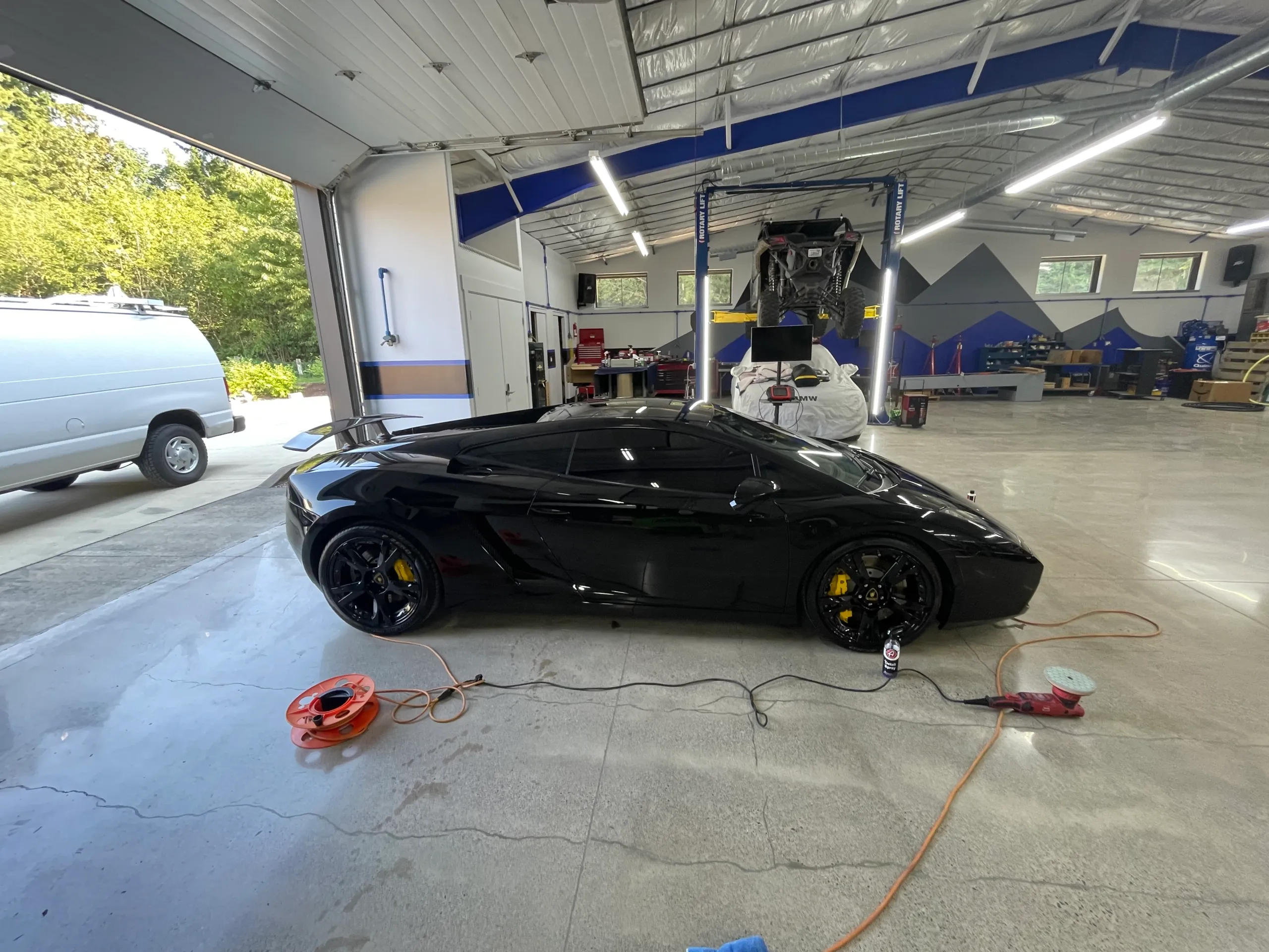 A black Lamborghini Gallardo mid-detail on the shop floor