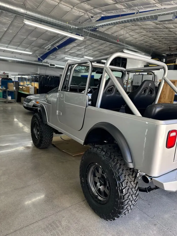 Silver restored Jeep CJ-8 Scrambler with a roll cage and off-road tyres inside a workshop