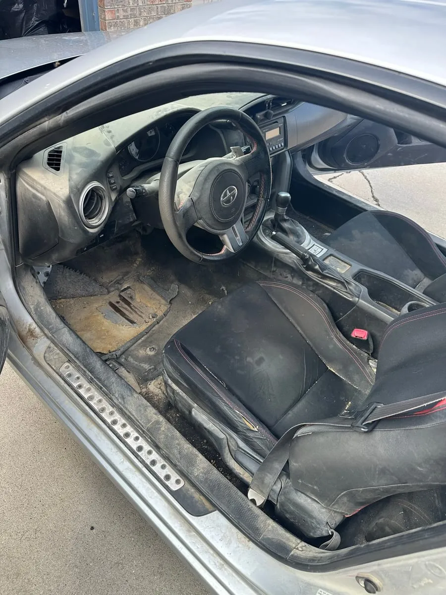 Scion FR-S driver's footwell seen through the open door, carpet and sill thick with dried dirt