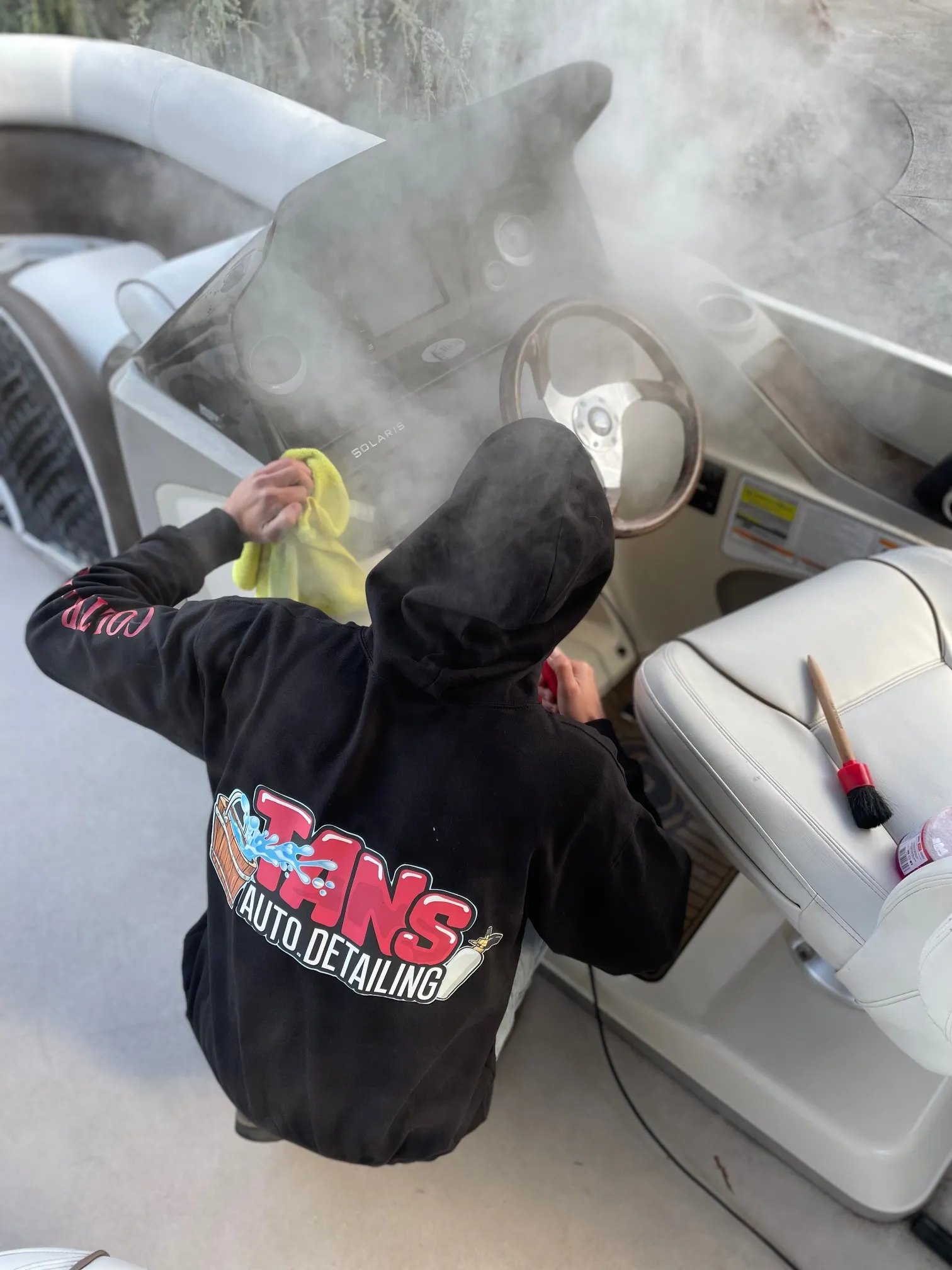 Tanner Coltrane in a Tan's Auto Detailing hoodie, steam-cleaning the dashboard of a pontoon boat