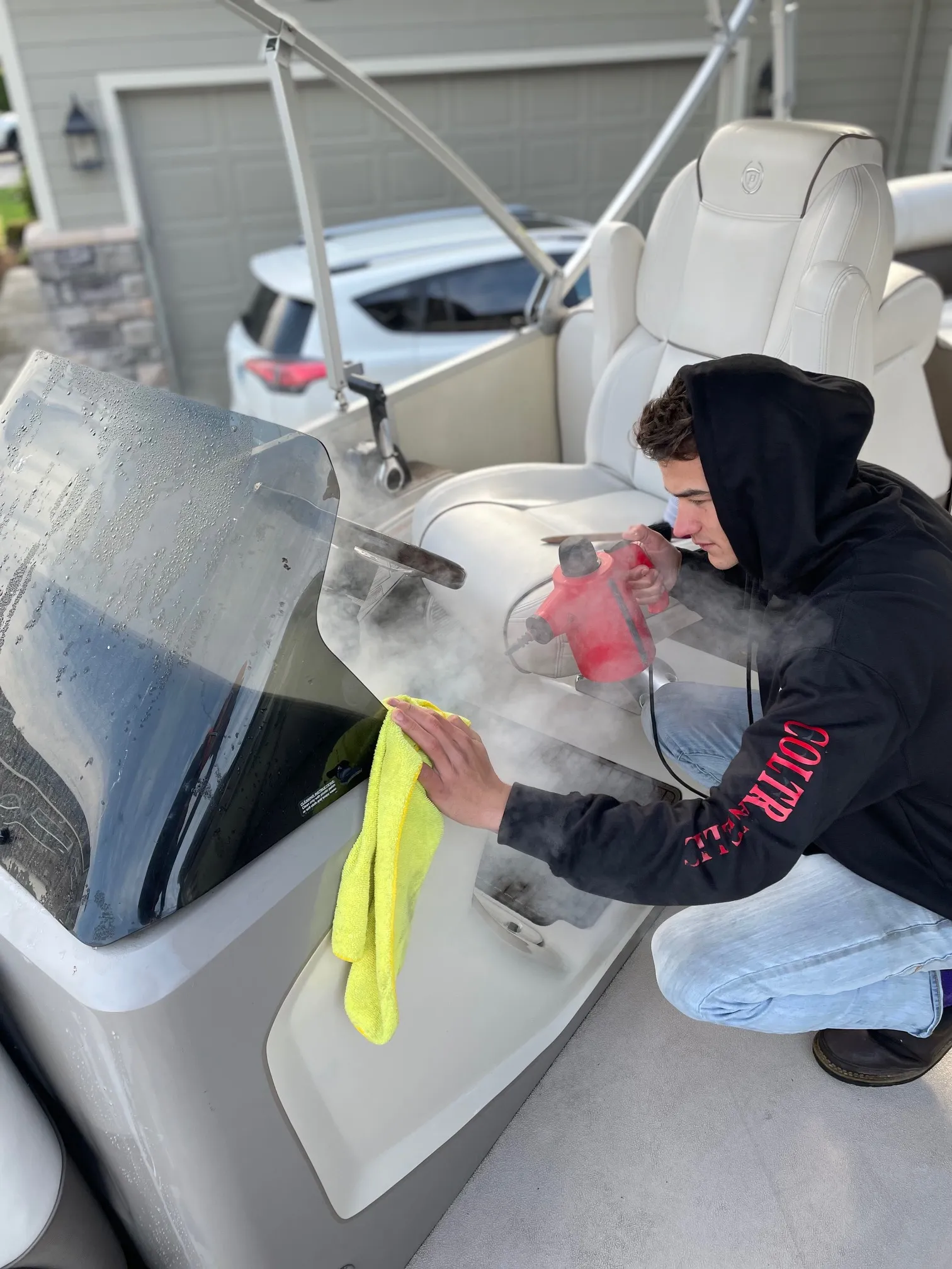Tanner steam-cleaning a pontoon boat seat on a customer's driveway
