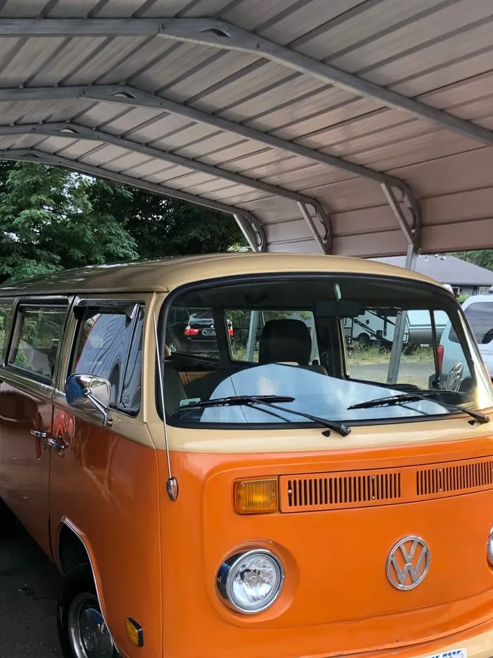Orange and cream Volkswagen Type 2 bus under a carport, chrome headlight and VW badge on the front panel
